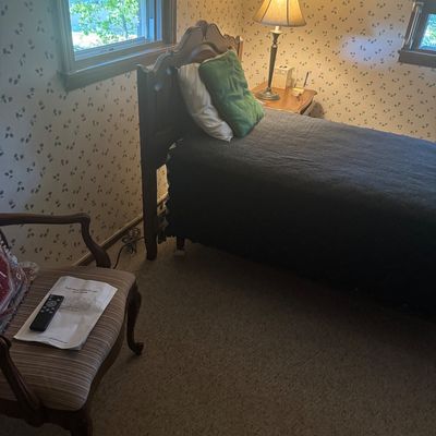 Sale Photo Thumbnail #25: Traditional wooden twin bed frame with a carved headboard, dark coverlet, and green accent pillow, accompanied by a matching nightstand and table lamp.