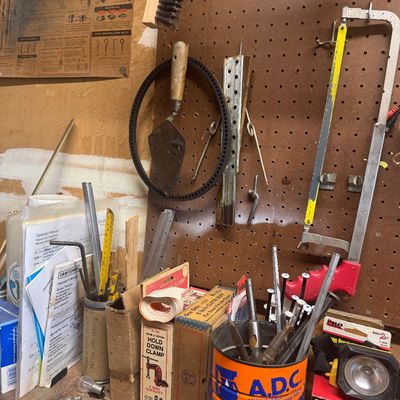 Sale Photo Thumbnail #102: Assorted workshop hand tools, hardware, and supplies arranged on a pegboard and workbench, including a hacksaw, mason's trowel, and Maxwell House coffee can organizer.