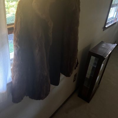 Sale Photo Thumbnail #36: Vintage mid-length brown fur coat hanging by a window.