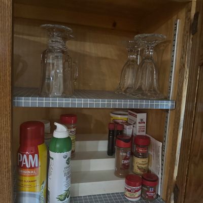 Sale Photo Thumbnail #234: Open wooden kitchen cabinet featuring clear glassware on the top shelf and cooking sprays alongside various McCormick spices on a tiered organizer below.