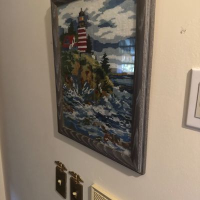 Sale Photo Thumbnail #40: Framed needlepoint art featuring a scenic lighthouse on a rocky coast, set in a rustic grey wood frame.