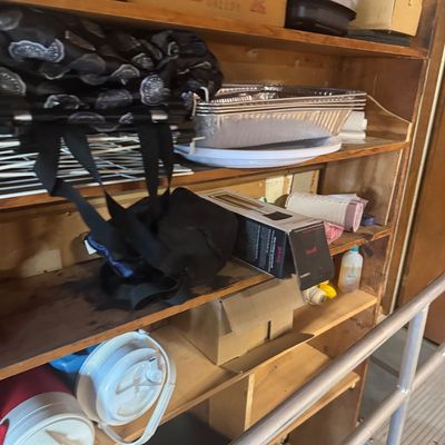 Sale Photo Thumbnail #97: Wooden shelving unit filled with household items, including disposable aluminum pans, plastic food storage containers, insulated water jugs, and various boxed goods.