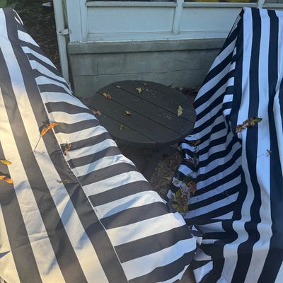 Sale Photo Thumbnail #135: Small round dark wood outdoor side table positioned between two patio chairs protected by black-and-white striped covers.