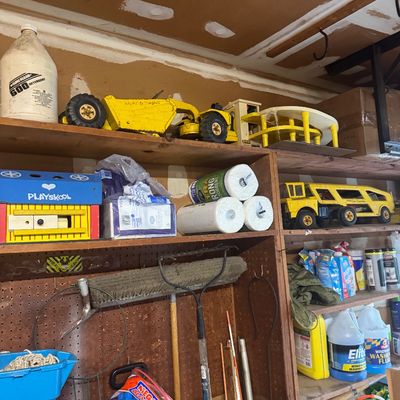 Sale Photo Thumbnail #90: Garage storage shelves featuring vintage Tonka pressed steel construction toys, a Playskool wooden barn, household cleaning supplies, and garden hand tools.