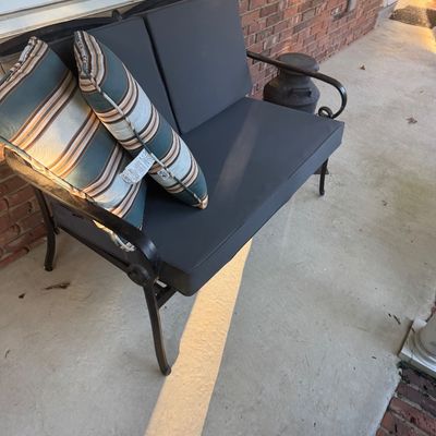 Sale Photo Thumbnail #119: Black wrought iron outdoor loveseat with dark grey seat and back cushions, accompanied by two striped accent pillows.