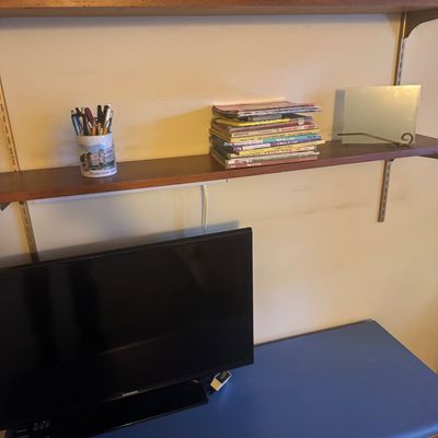 Sale Photo Thumbnail #52: Wall-mounted wooden shelving unit holding books, a pen holder, and a New York Yankees batting helmet above a small black Samsung flat-screen television.