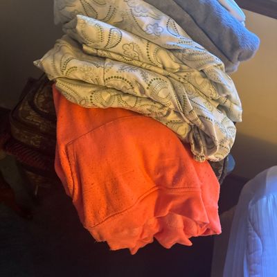 Sale Photo Thumbnail #47: Folded pile of assorted textiles, including a bright orange fleece sweatshirt, patterned paisley bedding or curtains, and plush grey towels.