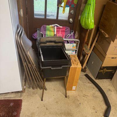 Sale Photo Thumbnail #92: Assorted household items in a storage area, including metal folding chairs, a black plastic tote bin, a wooden crate, and colorful lawn chairs.