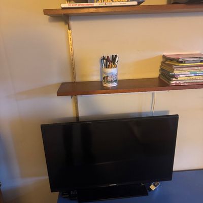 Sale Photo Thumbnail #53: Black Samsung flat-screen television on a blue desk surface, positioned below wall-mounted wooden shelves holding books and office supplies.