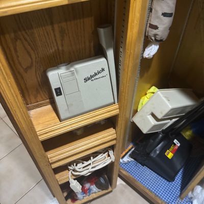 Sale Photo Thumbnail #236: Vintage Sidekick by Electrolux handheld vacuum attachment stored on a wooden shelving unit alongside household cleaning supplies.
