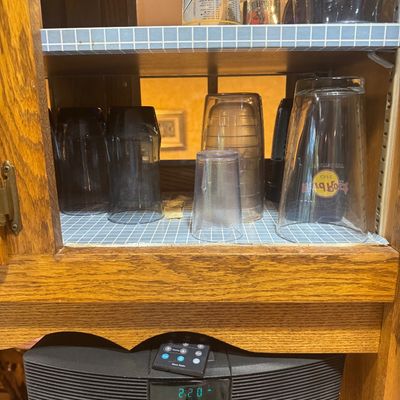 Sale Photo Thumbnail #215: Wooden hutch cabinet featuring shelves lined with blue grid paper holding assorted glassware, including a Hard Rock Cafe pint glass, positioned above a Bose Wave Radio.