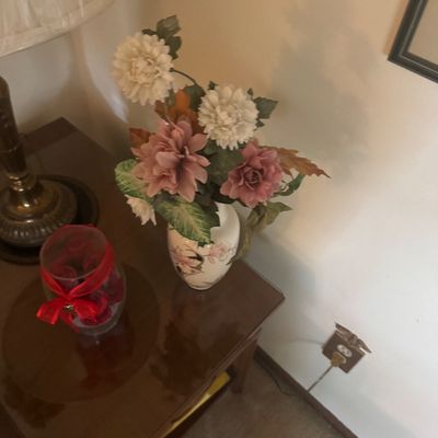 Sale Photo Thumbnail #173: Faux floral arrangement in a ceramic vase sitting on a dark wood end table alongside a glass jar tied with a red ribbon.
