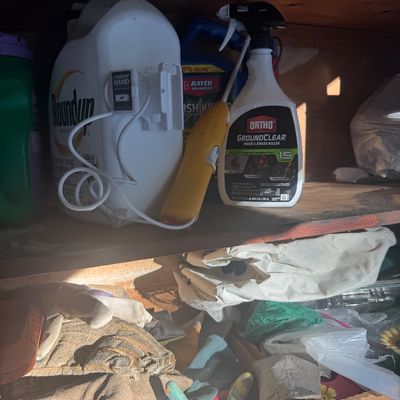 Sale Photo Thumbnail #80: Assorted lawn and garden chemicals, including Roundup with a comfort wand sprayer and Ortho GroundClear, stored on a shelf with various work gloves below.