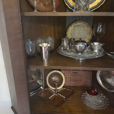 Sale Photo Thumbnail #208: Vintage wooden hutch displayed with various collectibles, including crystal glassware, silver-plated tea pieces, decorative trays, and mid-century wooden serving dishes.