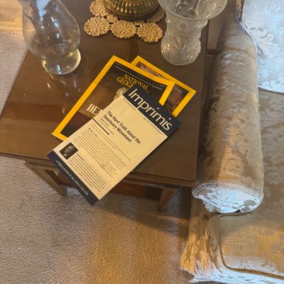 Sale Photo Thumbnail #166: Wooden end table featuring a glass top, paired with vintage glass vases, magazines, and a brass lamp base.