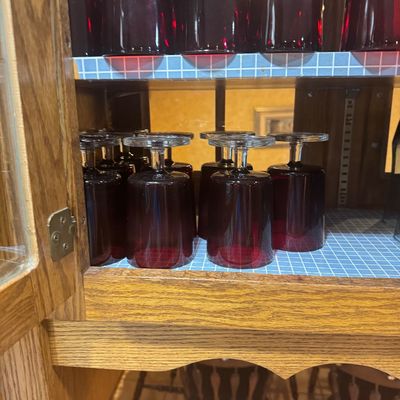 Sale Photo Thumbnail #221: Collection of ruby red glass wine goblets with clear stems, arranged inverted on wooden hutch shelves.