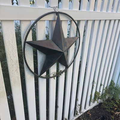 Sale Photo Thumbnail #124: Rustic metal Barn Star inside a twisted rope ring, hanging from a white picket fence in a Western or rustic decor style.