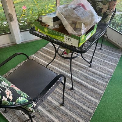 Sale Photo Thumbnail #10: Black wrought iron outdoor patio set with a mesh-top table, padded armchairs, and tropical floral accent pillows.