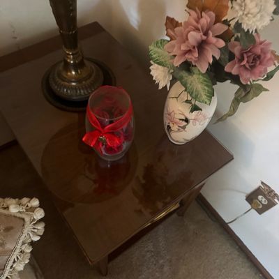Sale Photo Thumbnail #172: Dark wood side table featuring a brass-tone table lamp, a clear glass hurricane vase with red decorative accents, and a floral-patterned ceramic vase filled with artificial flowers.