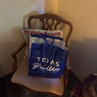 Sale Photo Thumbnail #48: Traditional wooden armchair with a carved backrest and striped upholstered seat, holding a throw pillow and a blue Texas Grown tote bag.