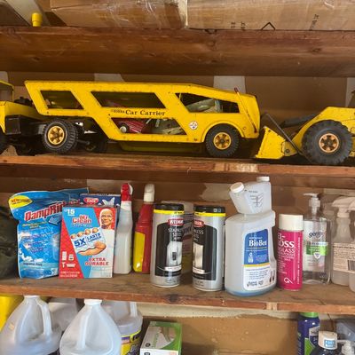 Sale Photo Thumbnail #87: Vintage yellow press-steel Tonka Car Carrier truck along with various household cleaning supplies and garage chemicals arranged on wooden shelving.