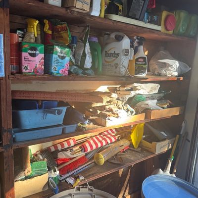 Sale Photo Thumbnail #81: Wooden garage shelving filled with various lawn, garden, and household supplies, including plant food, weed killers, cleaning products, and hand tools.