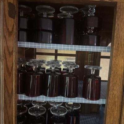 Sale Photo Thumbnail #224: Collection of mid-century ruby red goblet glasses with clear stems, stored upside down in a wooden hutch cabinet.