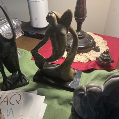 Sale Photo Thumbnail #194: Carved soapstone mermaid sculpture mounted on a black base, displayed alongside other decorative art objects and an Inuit Art Quarterly magazine.