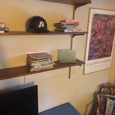 Sale Photo Thumbnail #55: Wall-mounted wooden shelving unit holding children's books and a New York Yankees mini batting helmet, alongside a framed Callaway Gardens art print.