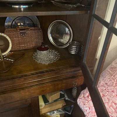 Sale Photo Thumbnail #207: Wooden display cabinet filled with glassware, silver-plated serving trays, stemware, and a small woven basket.