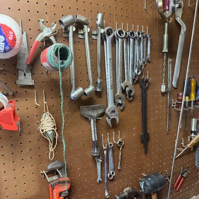 Sale Photo Thumbnail #104: Assorted vintage hand tools mounted on a pegboard, including Craftsman wrenches, socket handles, hammers, and a pipe wrench.