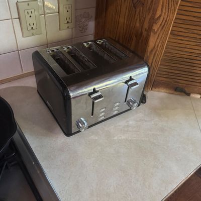 Sale Photo Thumbnail #233: Modern four-slot toaster in stainless steel and black trim, sitting on a kitchen countertop.