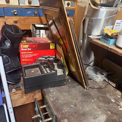 Sale Photo Thumbnail #103: Workshop workbench area featuring an EverStart battery charger, a medical walking boot, framed wooden panels, and various hand tools and hardware.