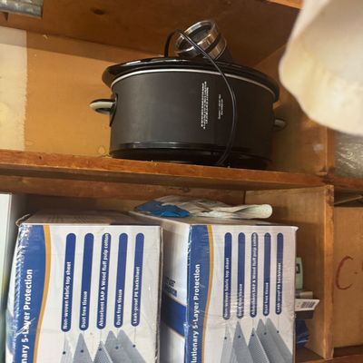 Sale Photo Thumbnail #98: Black Crock-Pot slow cooker sitting on a wooden shelf above two boxes of 5-layer protection underpads.