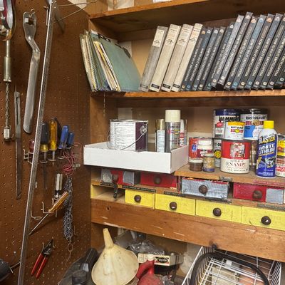 Sale Photo Thumbnail #107: Workshop shelving loaded with a complete vintage How-To-Do-It encyclopedia set, paint cans, spray lubricants, and assorted hand tools organized on a pegboard.
