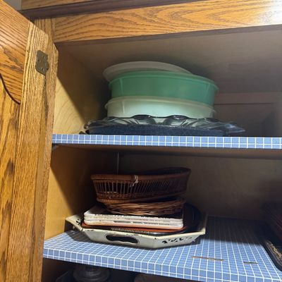 Sale Photo Thumbnail #244: Wooden kitchen cabinet filled with various household items, including vintage plastic pie carriers, glass pie dishes, woven baskets, and serving trays.