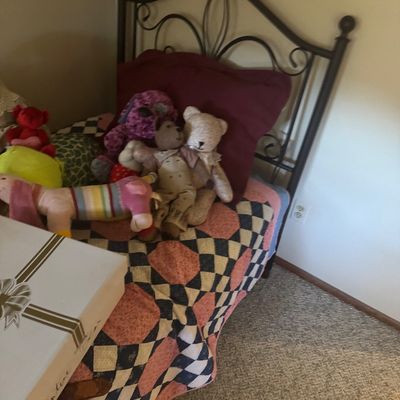 Sale Photo Thumbnail #64: Twin bed featuring a dark wrought iron scrollwork headboard, layered with a vintage patchwork quilt and various plush stuffed animals.