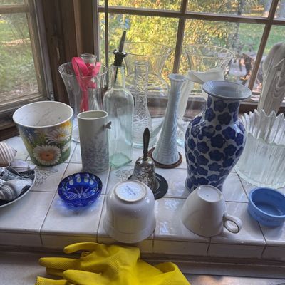 Sale Photo Thumbnail #228: Assortment of glassware and ceramics displayed on a tiled windowsill, including a blue and white Asian-style floral vase, clear glass vases, a milk glass bud vase, and small pottery items.
