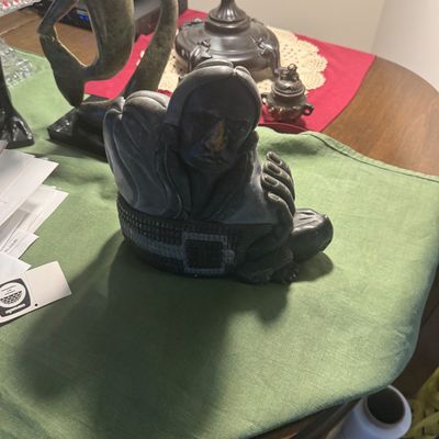 Sale Photo Thumbnail #195: Inuit carved dark stone sculpture depicting a stylized human figure alongside additional figurines and decor on a table runner.