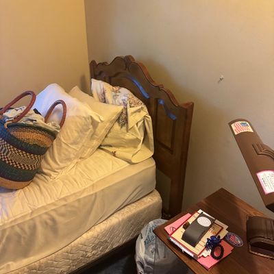 Sale Photo Thumbnail #60: Twin bed featuring a carved wooden headboard, accompanied by a woven Bolga basket bag and a wooden nightstand with assorted small accessories.