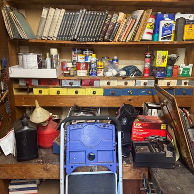 Sale Photo Thumbnail #108: Wooden workshop shelving unit filled with how-to books, paint cans, solvents, and small parts drawers, alongside a folding step stool and various garage supplies.