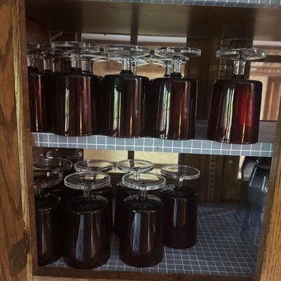 Sale Photo Thumbnail #220: Collection of vintage dark ruby red goblet glassware stored upside down on two wooden cabinet shelves.