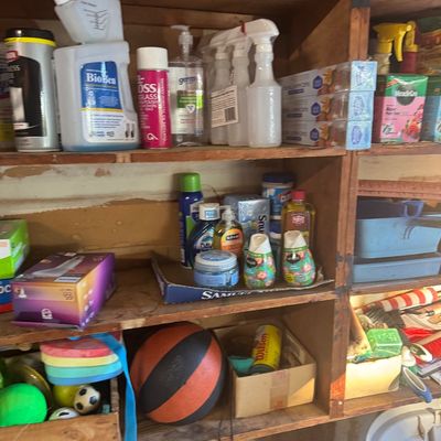 Sale Photo Thumbnail #83: Wooden garage shelving units stocked with various cleaning supplies, household chemicals, sports balls, and miscellaneous goods.