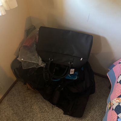 Sale Photo Thumbnail #66: Collection of luggage and bags stacked in a room, including a black duffel bag with handles and attached retail tag.