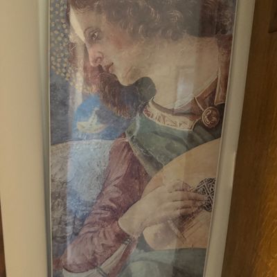 Sale Photo Thumbnail #153: Framed vertical art print depicting a Renaissance-style angelic figure playing a lute, presented under glass in a simple white frame.