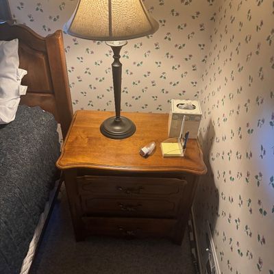 Sale Photo Thumbnail #18: French Provincial style wooden nightstand with three drawers and bail handles, paired with a metal buffet-style table lamp.