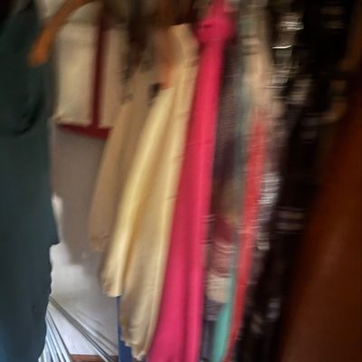 Sale Photo Thumbnail #33: Selection of assorted vintage clothing, including a bright pink sweater and light yellow jacket, hanging in a closet.