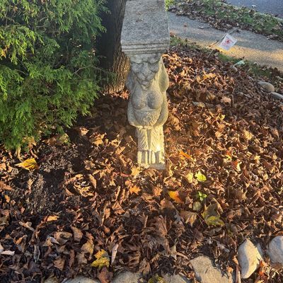 Sale Photo Thumbnail #122: Weathered concrete garden pedestal featuring a carved gargoyle or grotesque figure, positioned outdoors near foliage.