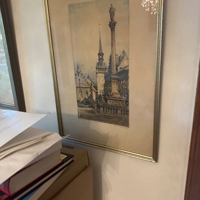 Sale Photo Thumbnail #199: Framed architectural watercolor print featuring a European city square with a tall monument and church spire, presented in a thin gold metal frame with matting.