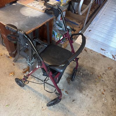 Sale Photo Thumbnail #109: Burgundy four-wheeled rollator walker featuring a padded seat, ergonomic hand grips with brakes, and a front curved backrest.